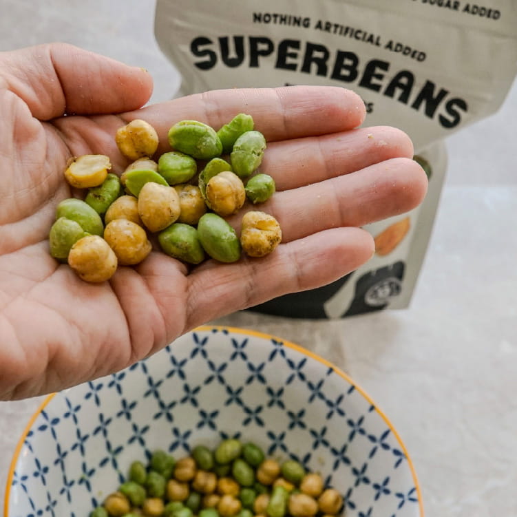 Hand holding green and yellow beans with a 'Superbeans' package in the background