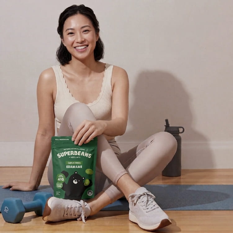 Woman sitting on a yoga mat with a package of Superbeans Edamame in a home setting